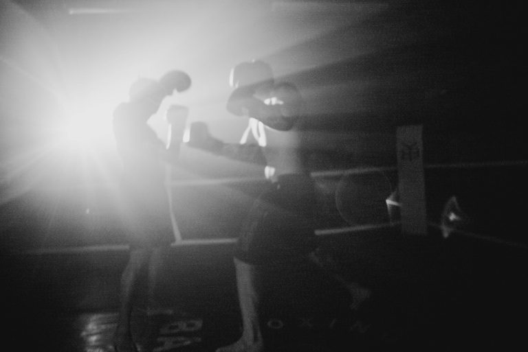 A powerful black and white image of boxers sparring with dramatic lighting in a gym setting.